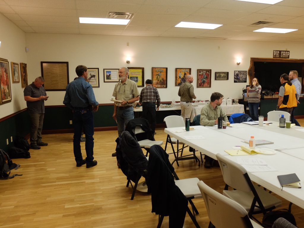A meeting room with framed vintage posters on the walls. Several people gather around folding tables with papers and drinks.